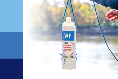 A hand holding up a water sampler with a river in the background